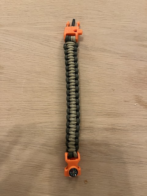 Her er clipsen i en fantastisk oransje farge. Her ser du detaljene til clipsen, med tennstål og fløyte øverst. kompass og kniv til tennstålet nederst